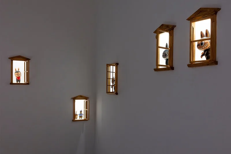 Personnages miniatures dans des fenêtres illuminées sur un mur blanc.