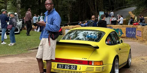 Homme appuyé sur une voiture Porsche jaune lors d'un événement en plein air.