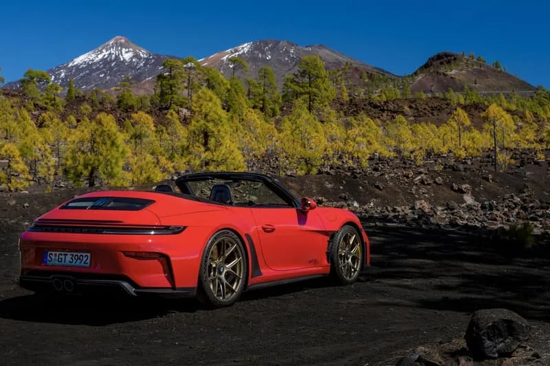 Voiture rouge sur route montagneuse avec arbres et montagnes enneigées