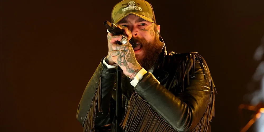 Chanteur tatoué en veste à franges avec micro sur scène.