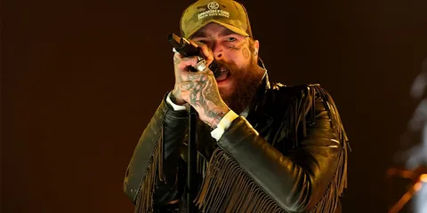 Chanteur tatoué en veste à franges avec micro sur scène.