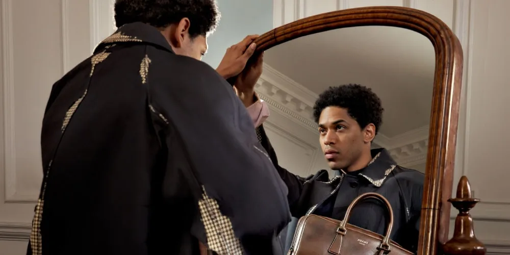 Homme regardant dans un miroir avec un manteau et sac brun.