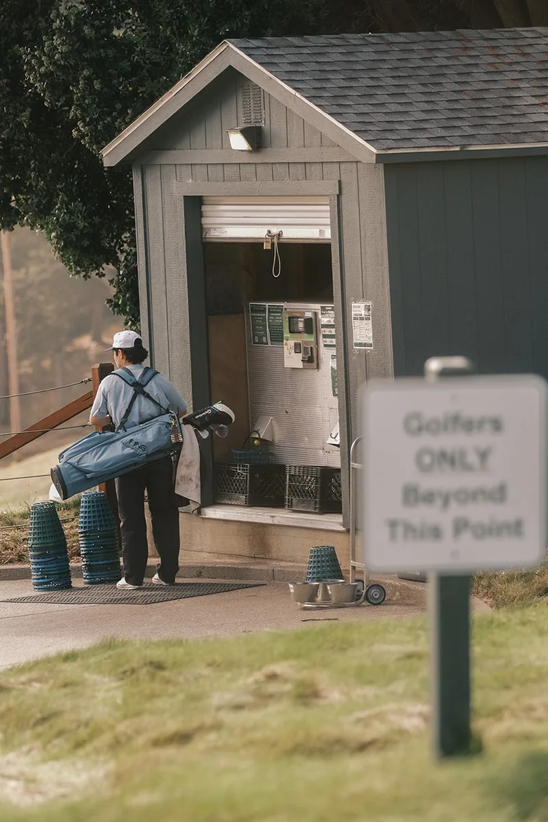 Personne avec des clubs de golf près d'une cabane et d'un panneau 'Golfeurs Seulement'.