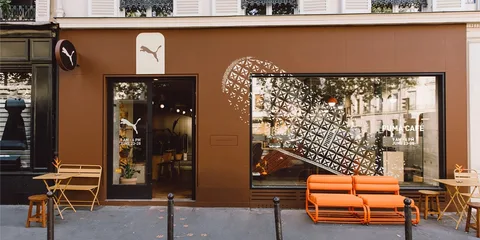 Façade de café Puma à Paris avec chaises orange et marron.