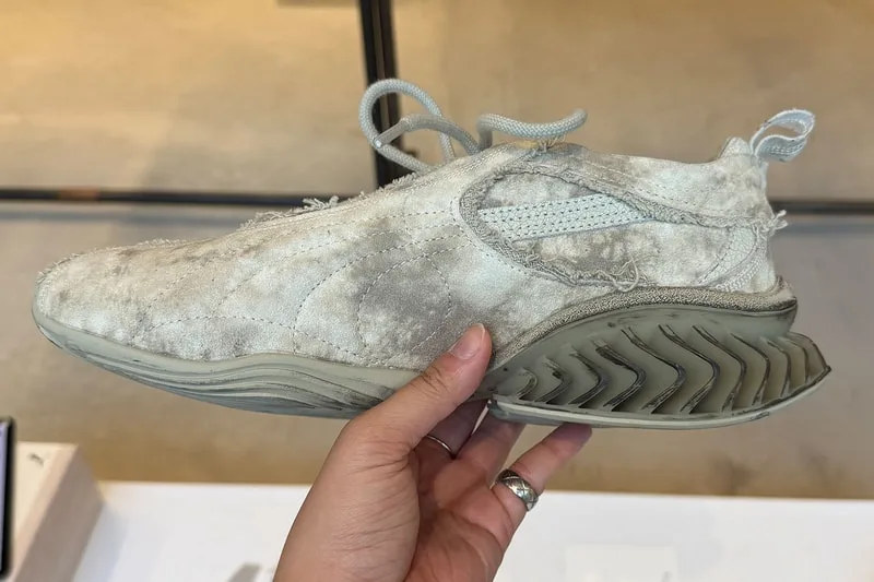 Main tenant une chaussure de sport beige usée au design unique.