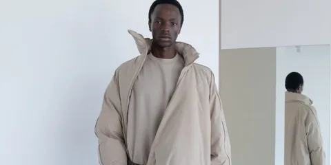Homme portant une veste beige avec un col haut devant un miroir.