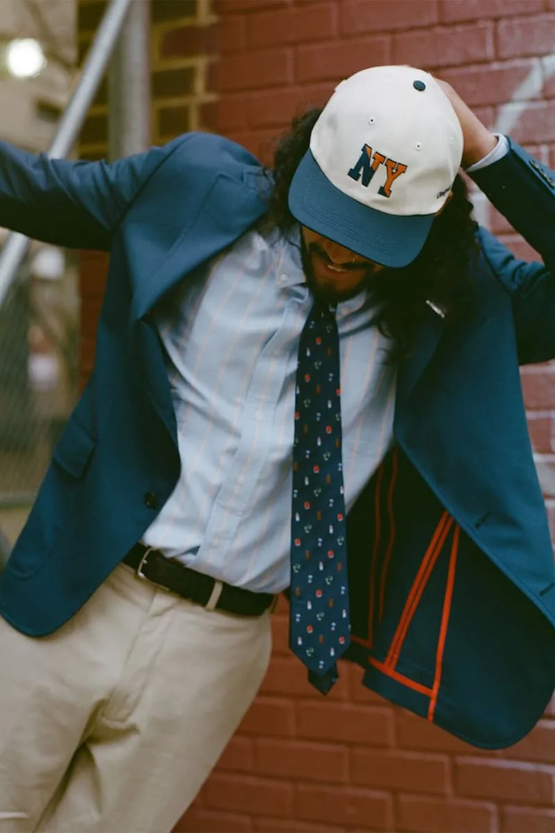 Homme en costume bleu, chemise rayée, cravate à motifs, casquette NY.