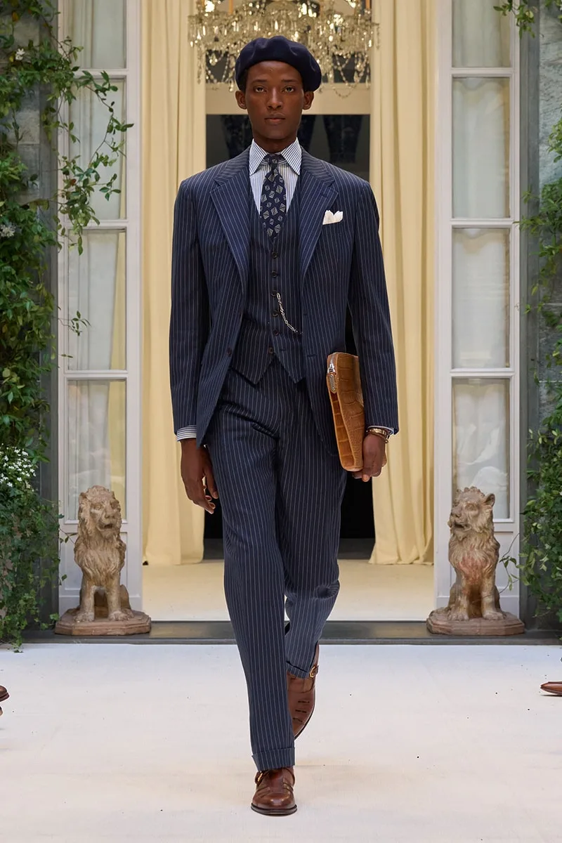 Homme élégant en costume rayé bleu défilant dans un cadre luxueux.