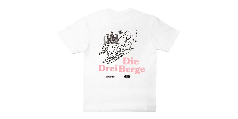 T-shirt blanc avec illustration ville et texte 'Die Drei Berge' en rose.