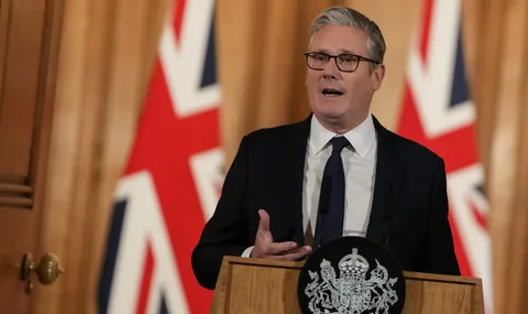 Personne parlant devant des drapeaux britanniques et un pupitre.