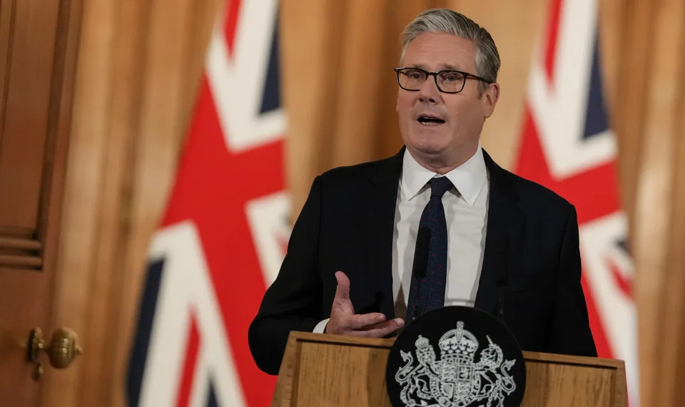 Personne parlant devant des drapeaux britanniques et un pupitre.