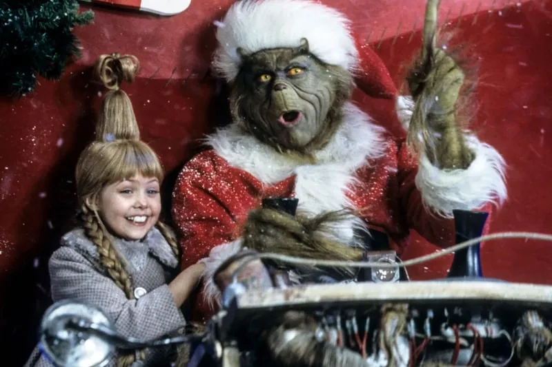 Fille avec coiffure unique assise avec un personnage en costume de Père Noël Grinch.
