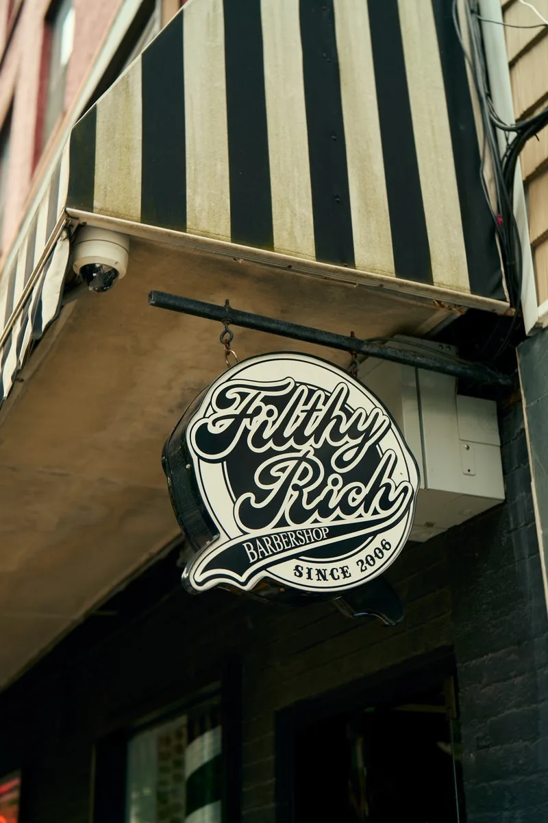 Enseigne de barbier avec texte Filthy Rich et auvent rayé.