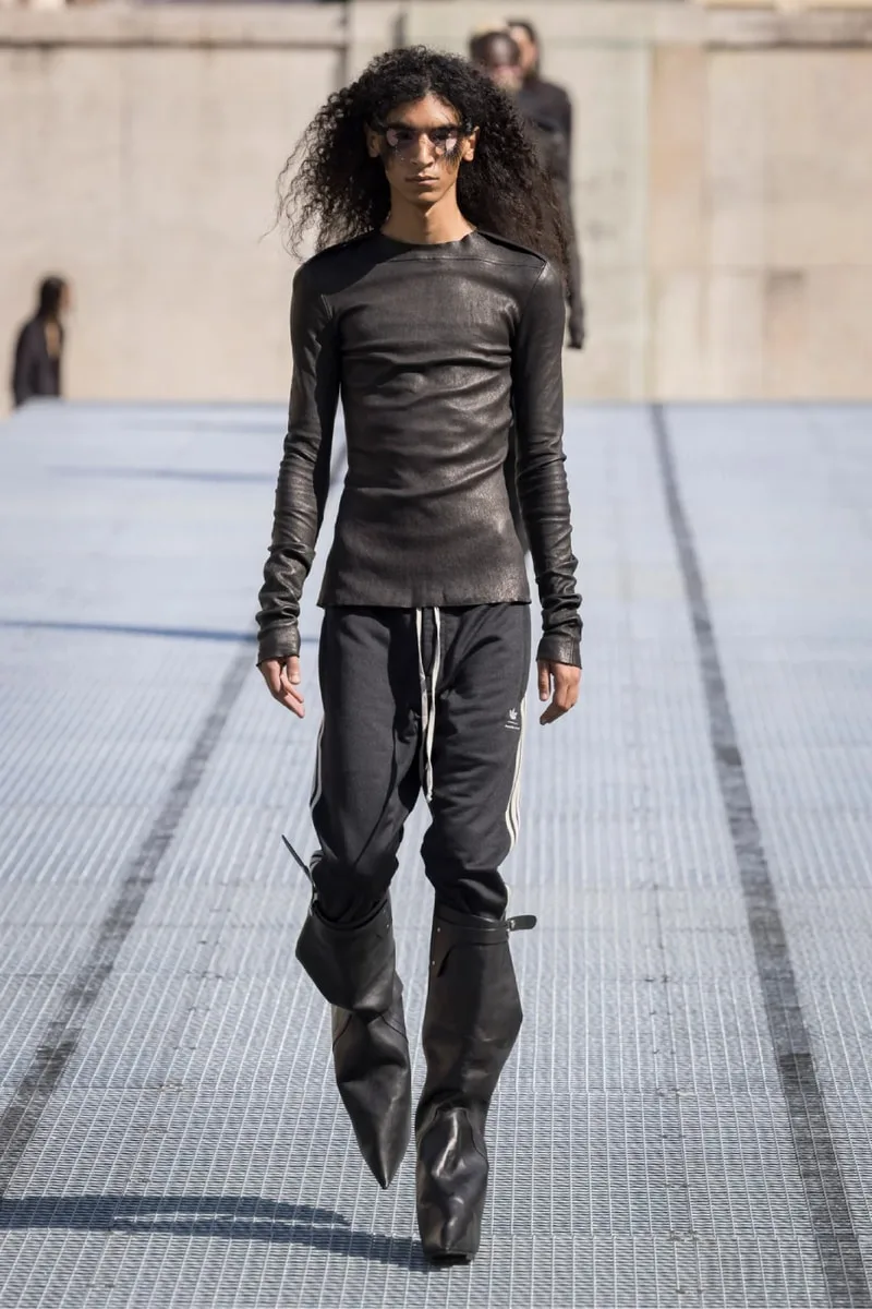 Personne défilant en tenue noire avec bottes volumineuses.