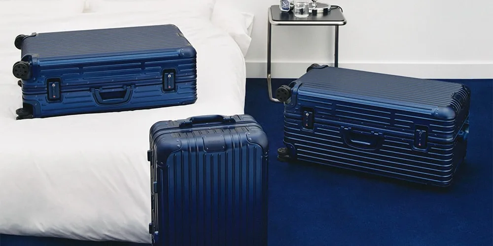 Trois valises bleues sur un sol bleu et un lit blanc.