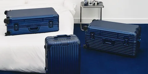 Trois valises bleues sur un sol bleu et un lit blanc.