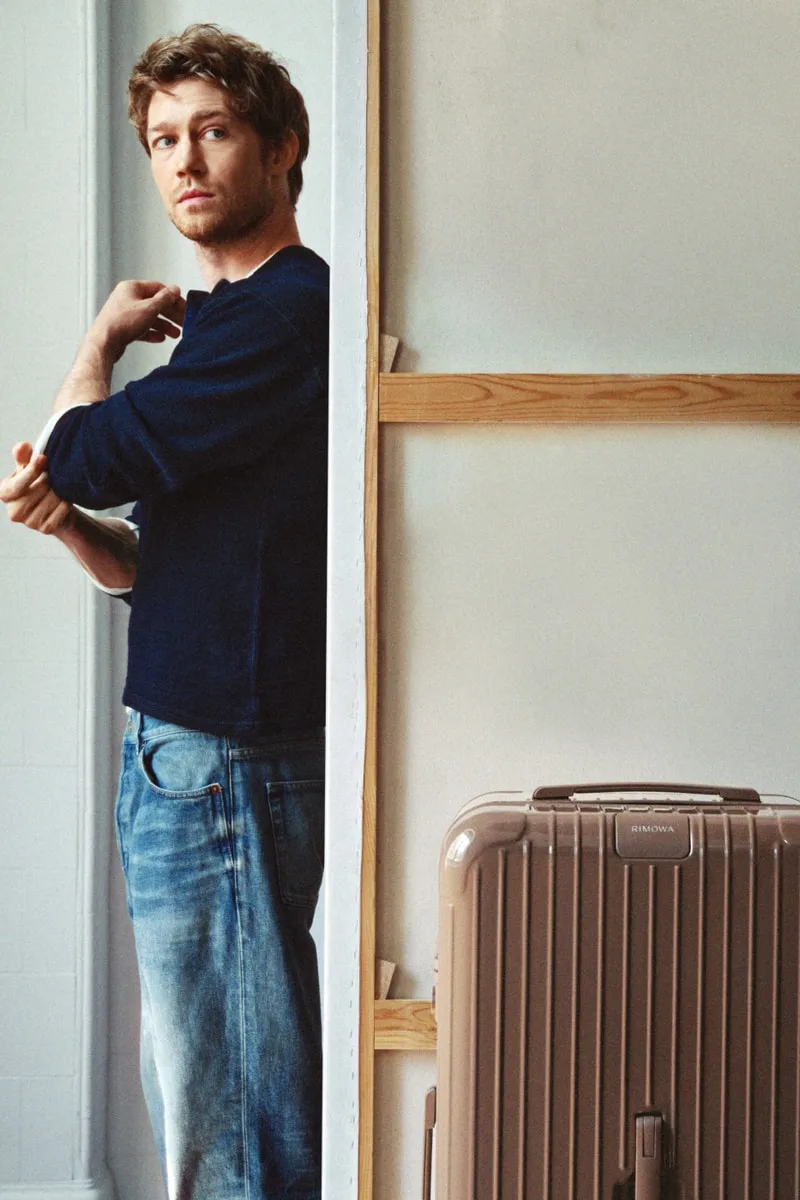 Homme près d'une valise beige dans une pièce minimaliste.