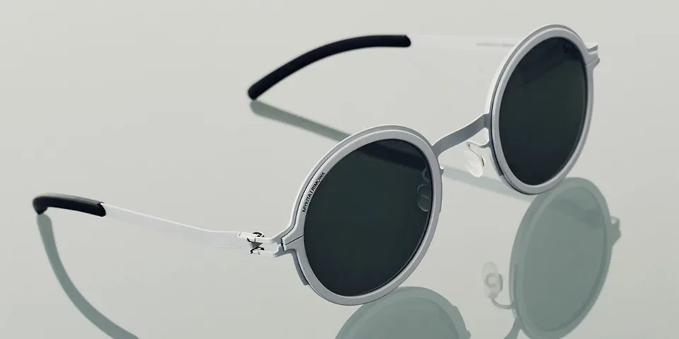 Lunettes de soleil rondes à monture argentée posées sur une surface réfléchissante.