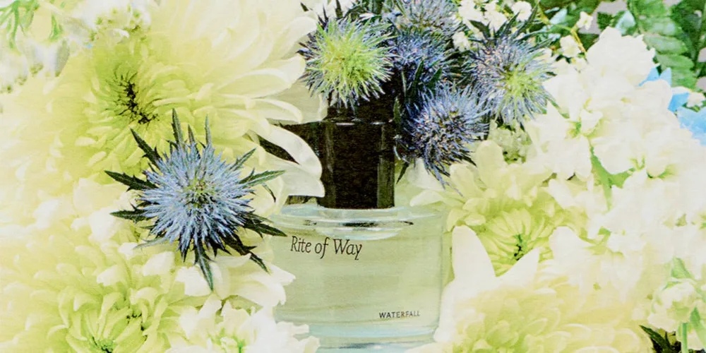 Bouteille de parfum Rite of Way entourée de fleurs blanches et bleues.