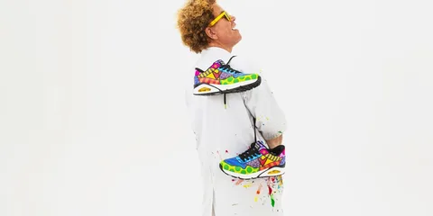 Homme avec lunettes jaunes et chaussures colorées, fond blanc.