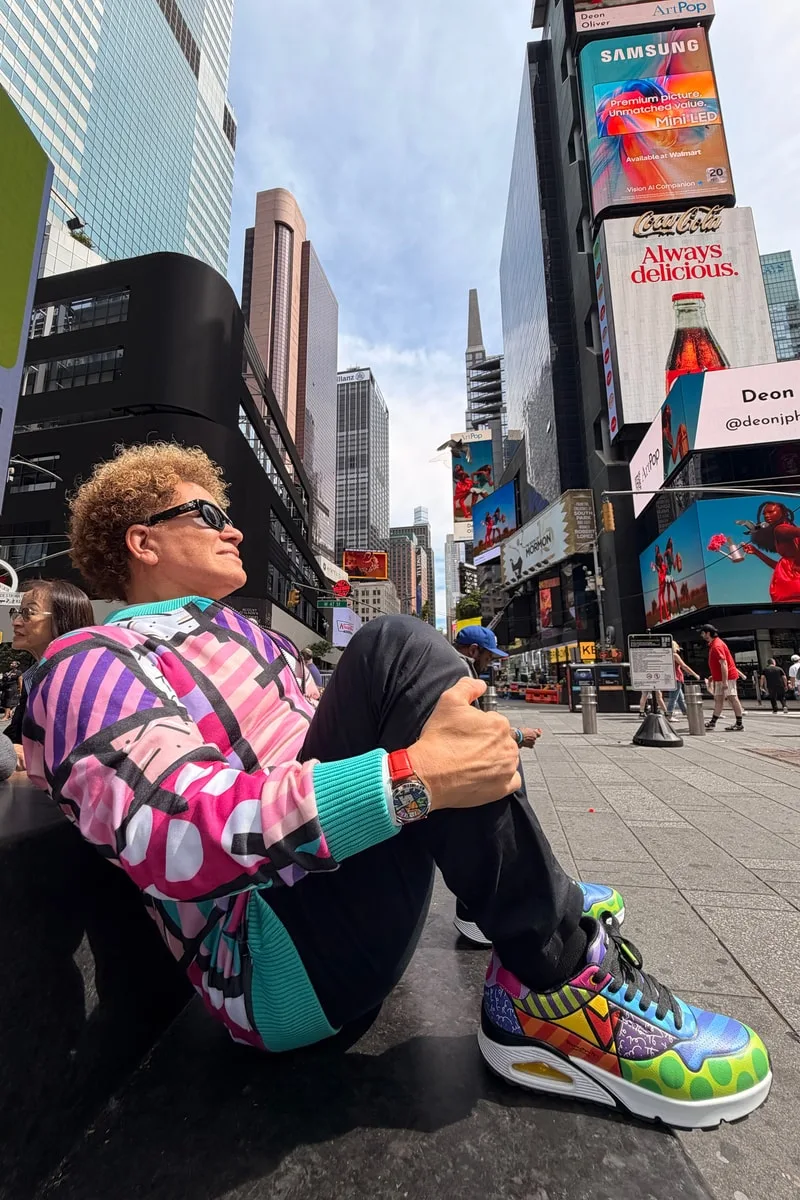 Homme en vêtements colorés assis à Times Square avec des baskets vives.