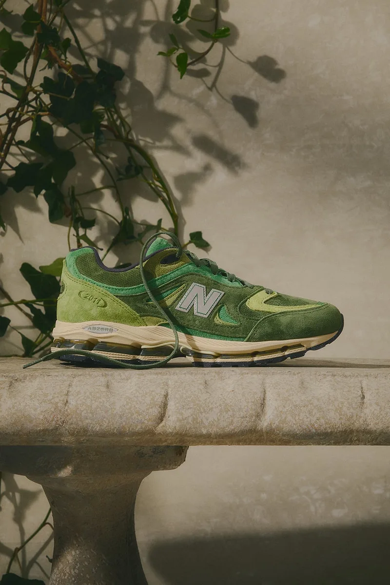 Chaussure verte New Balance sur une table en pierre, feuillages en arrière-plan.