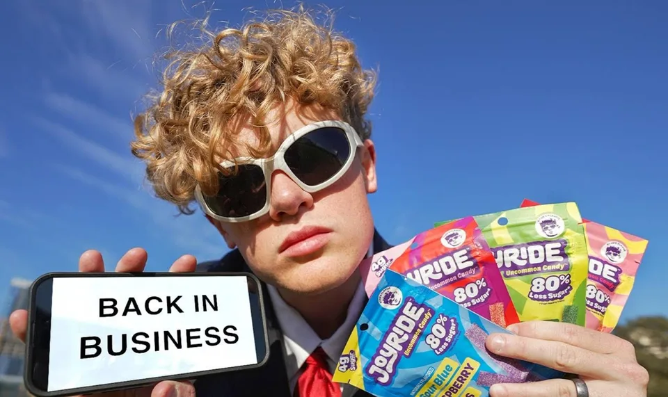 Homme avec lunettes tenant friandises et téléphone 'Back in Business'.
