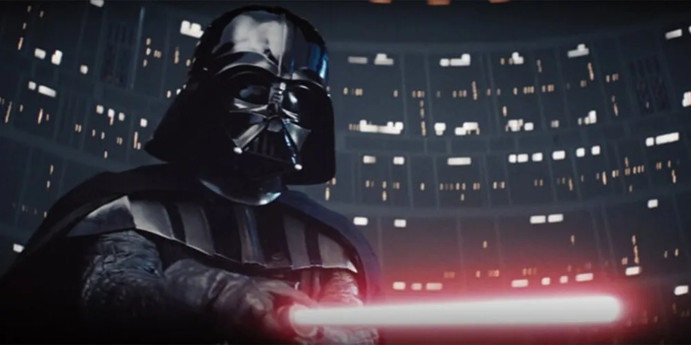 Personnage en armure noire avec un sabre laser rouge, dans un environnement sombre.
