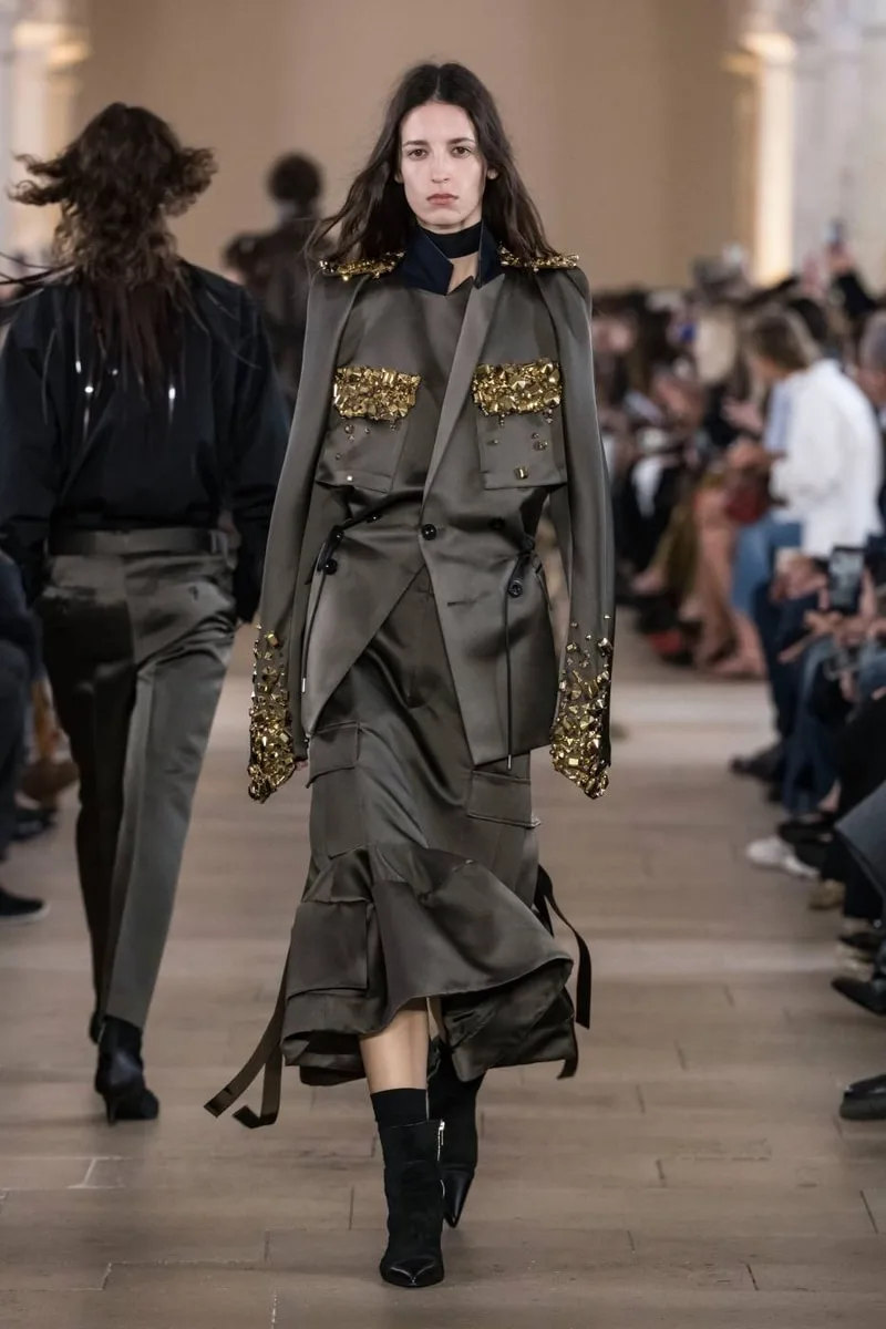 Mannequin défilant en tenue chic avec détails dorés.