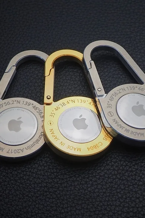 Trois mousquetons Apple en métal gris et doré sur fond noir.