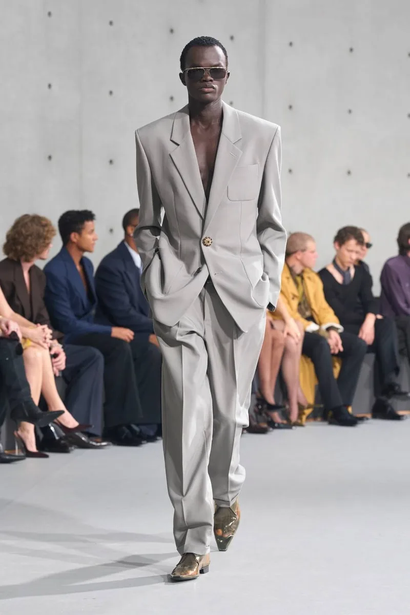 Modèle défilant avec un costume gris devant le public assis.