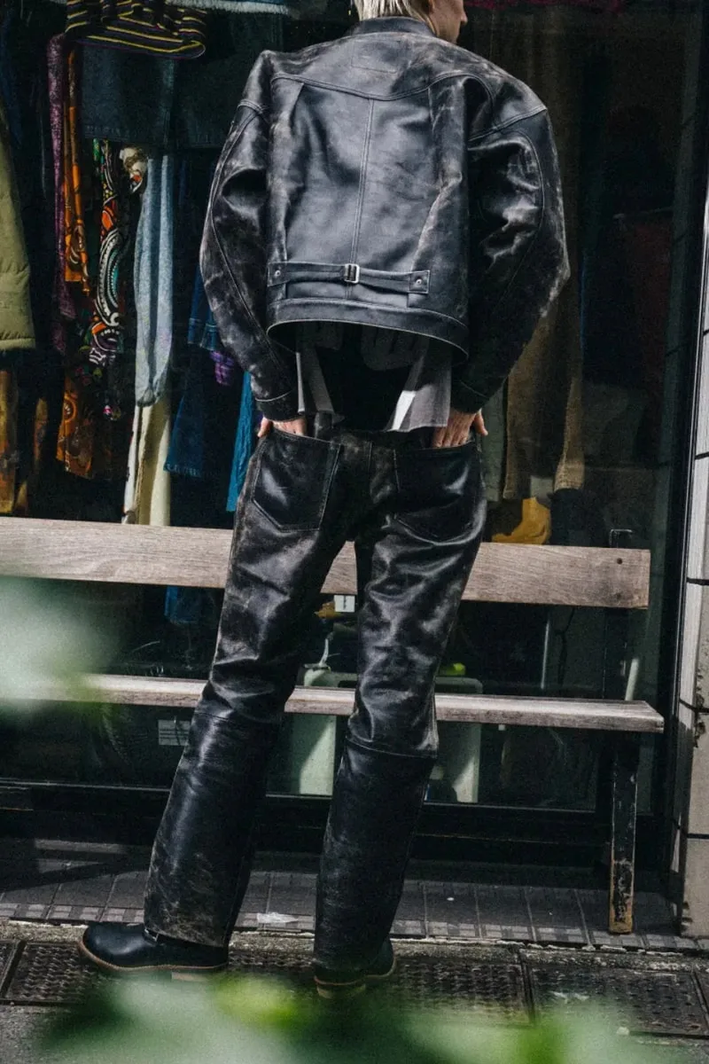 Personne en blouson et pantalon en cuir sombre devant une vitrine.