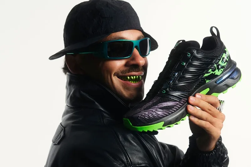 Homme avec lunettes et grille tient une chaussure noire et verte.