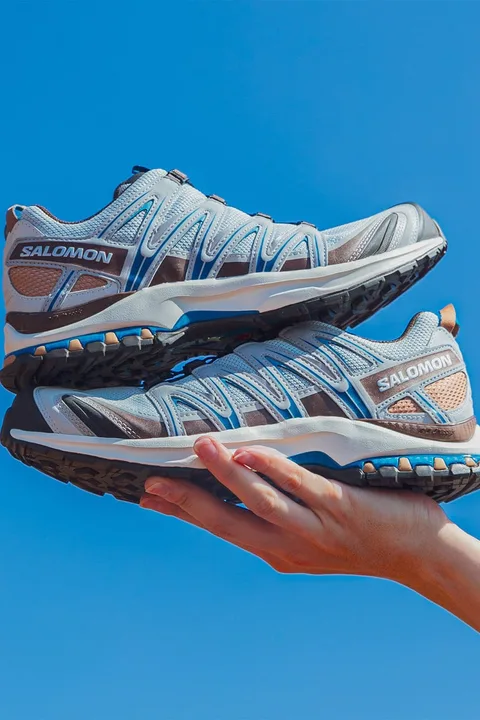 Deux chaussures Salomon bleu clair tenues en l'air avec un ciel bleu en fond.