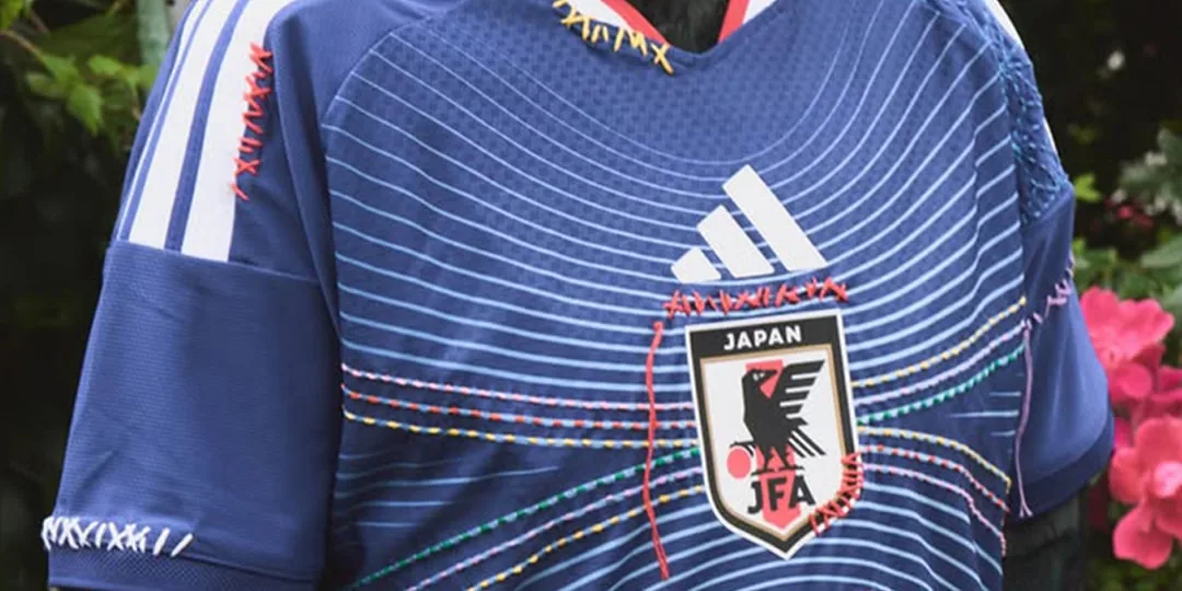 Maillot de football bleu avec logo JFA brodé en couleurs vives.
