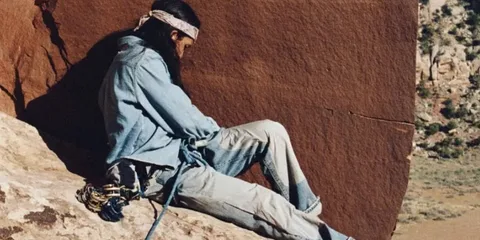 Homme assis sur une falaise rocheuse, vêtu de vêtements décontractés.