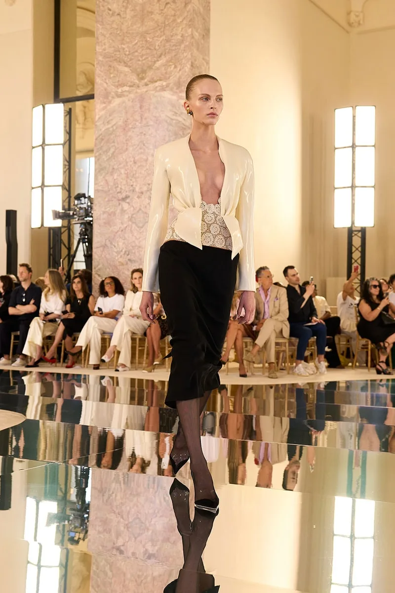 Défilé de mode avec mannequin et tenue élégante sur podium à intérieur chic.