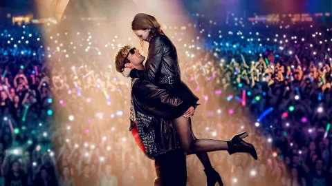 Un couple sur scène, l'homme porte la femme, arrière-plan de concert vibrant.
