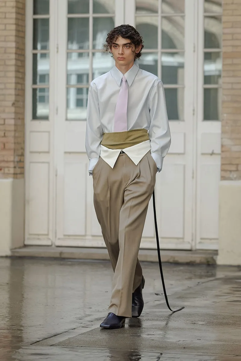 Homme en chemise et pantalon beige, portant une ceinture verte.