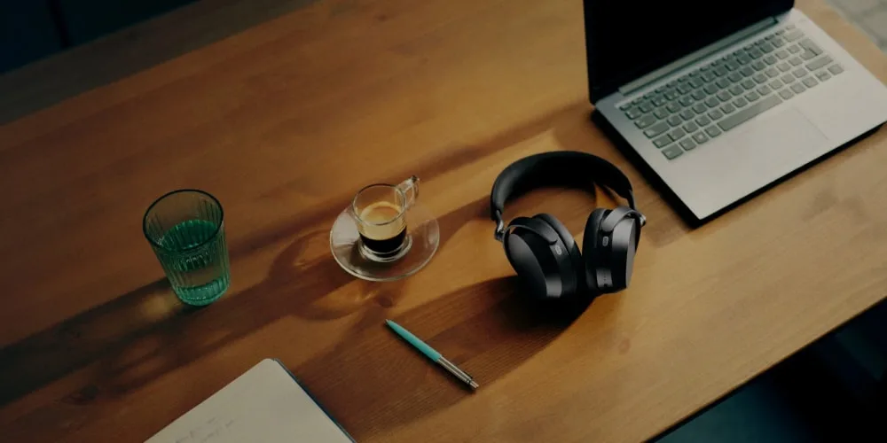 Bureau avec PC portable, casque, café, verre et carnet avec stylo.