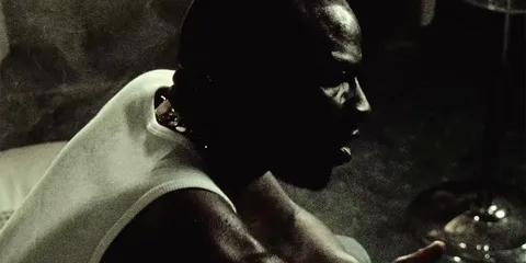 Homme de profil assis dans une pièce sombre.