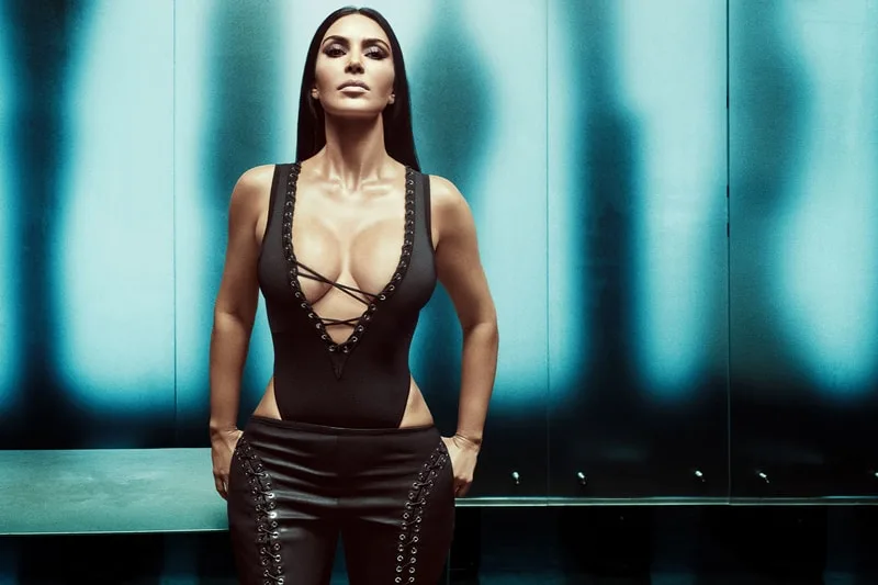 Femme en tenue noire, fond bleu lumineux, pose confiante.