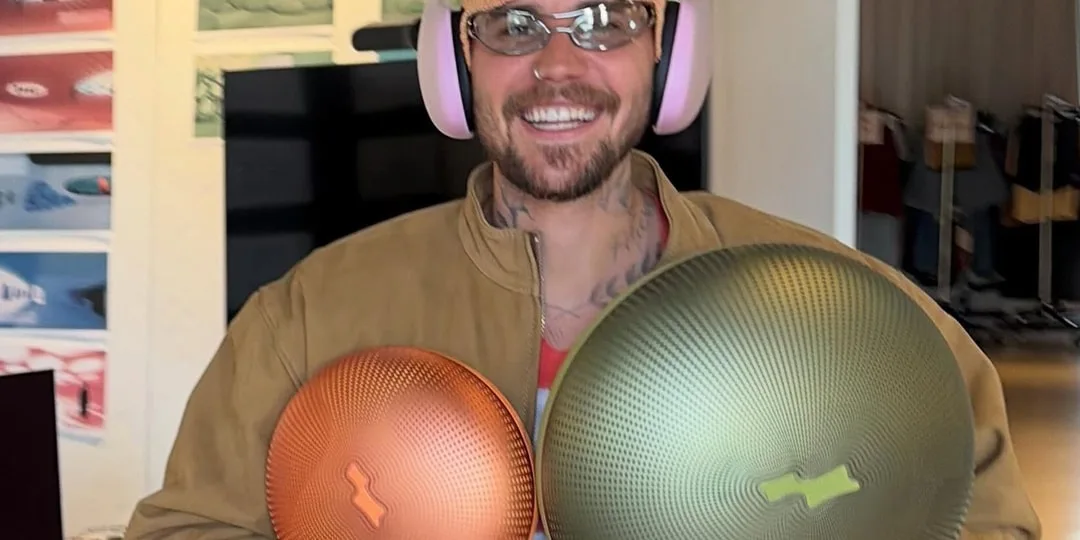 Homme souriant avec casquette, écouteurs et deux disques colorés, intérieur moderne