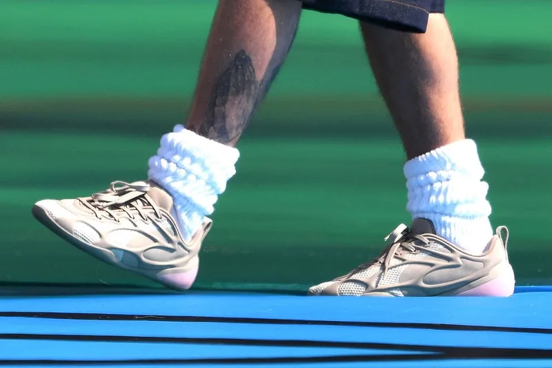 Pieds portant des chaussures beige et chaussettes blanches sur fond bleu-vert.