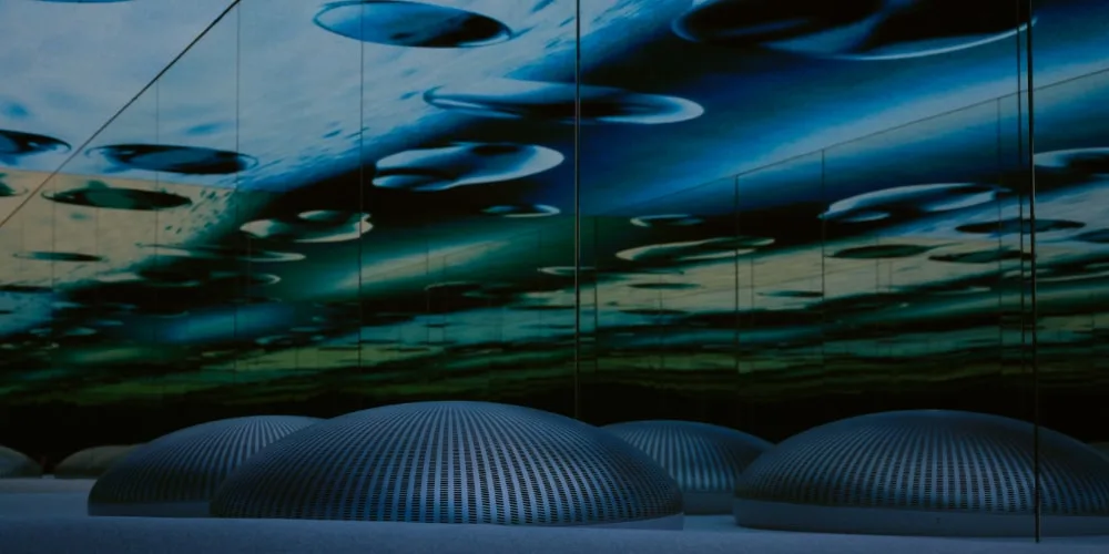 Installation immersive avec un plafond miroir bleu et des dômes lumineux.
