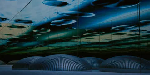 Installation immersive avec un plafond miroir bleu et des dômes lumineux.
