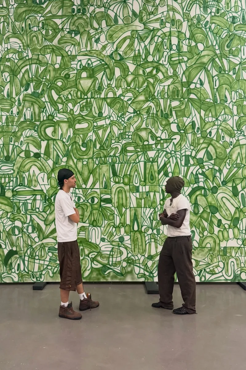 Deux personnes discutent devant une peinture murale verte abstraite.