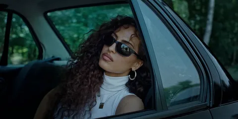 Femme avec lunettes de soleil dans une voiture, regardant dehors.