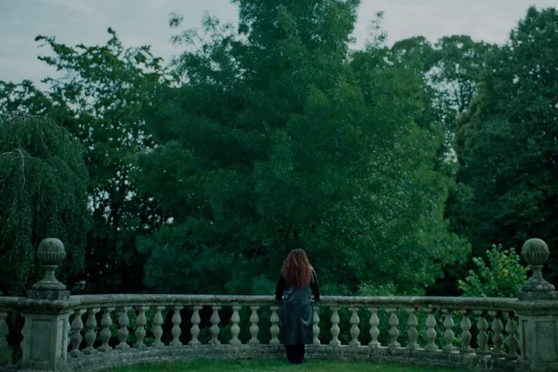 Personne debout devant une balustrade en pierre dans un jardin verdoyant.