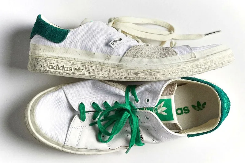 Deux baskets blanches avec des détails verts et logo Adidas.